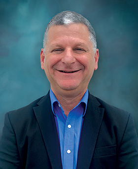 Smiling older man, with short cropped hair, dressed in a blazer and blue shirt